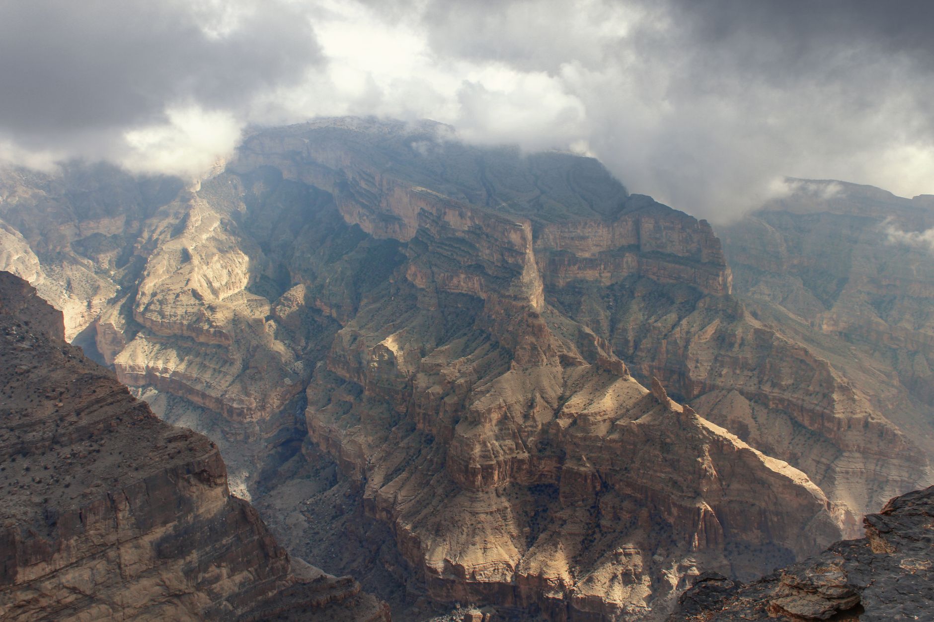 Vue aérienne des reliefs escarpés du Jebel Shams sous des nuages spectaculaires, Oman