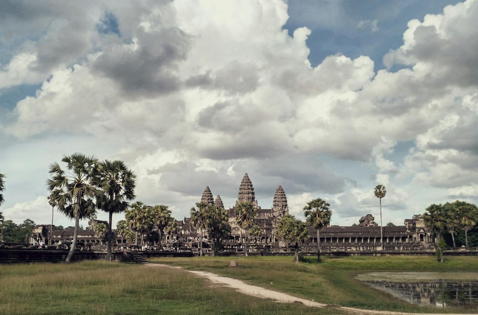 Temple d'Angkor Wat entouré de palmiers sous un ciel nuageux spectaculaire