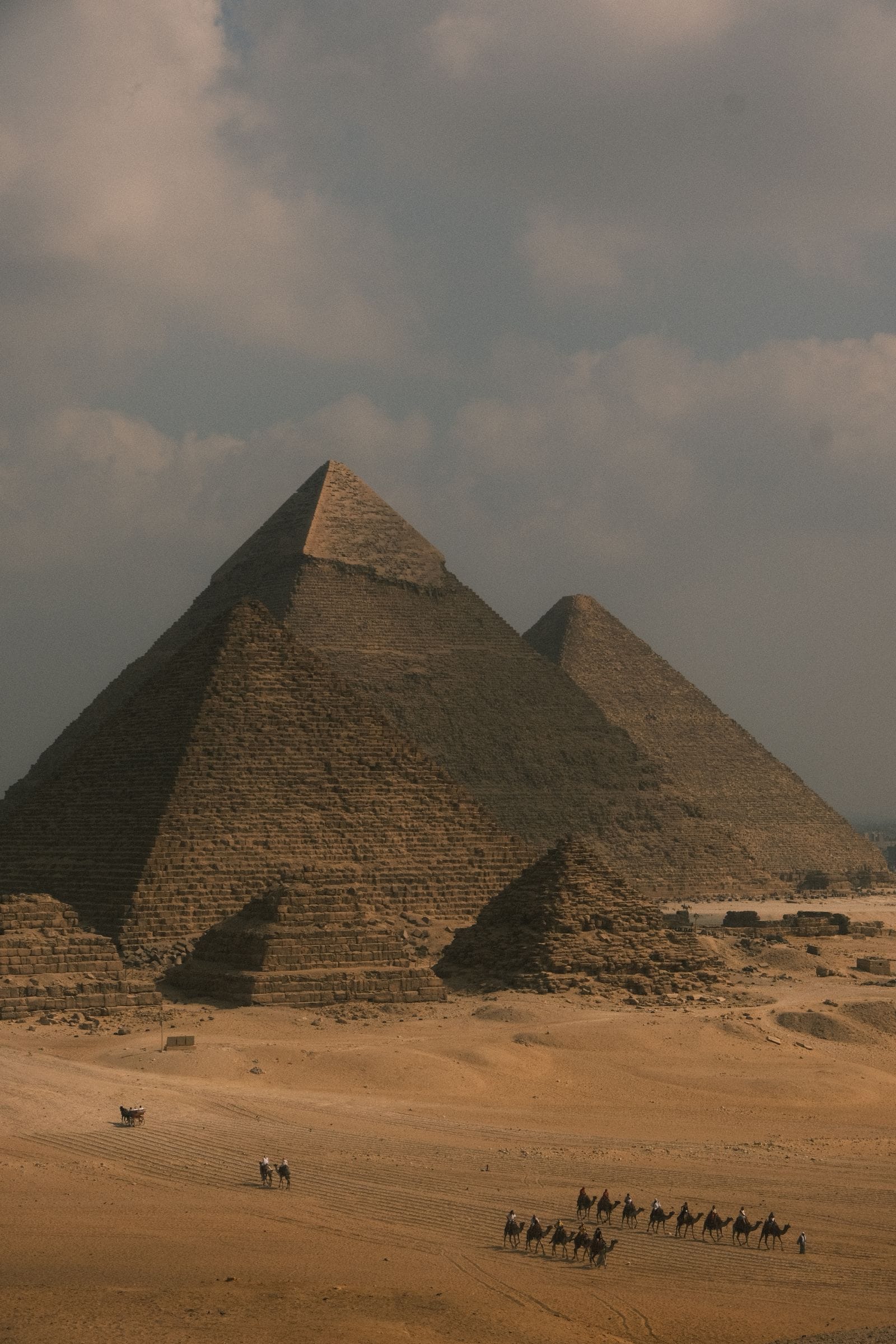 Pyramides de Gizeh avec caravane de chameaux dans le désert sous un ciel nuageux