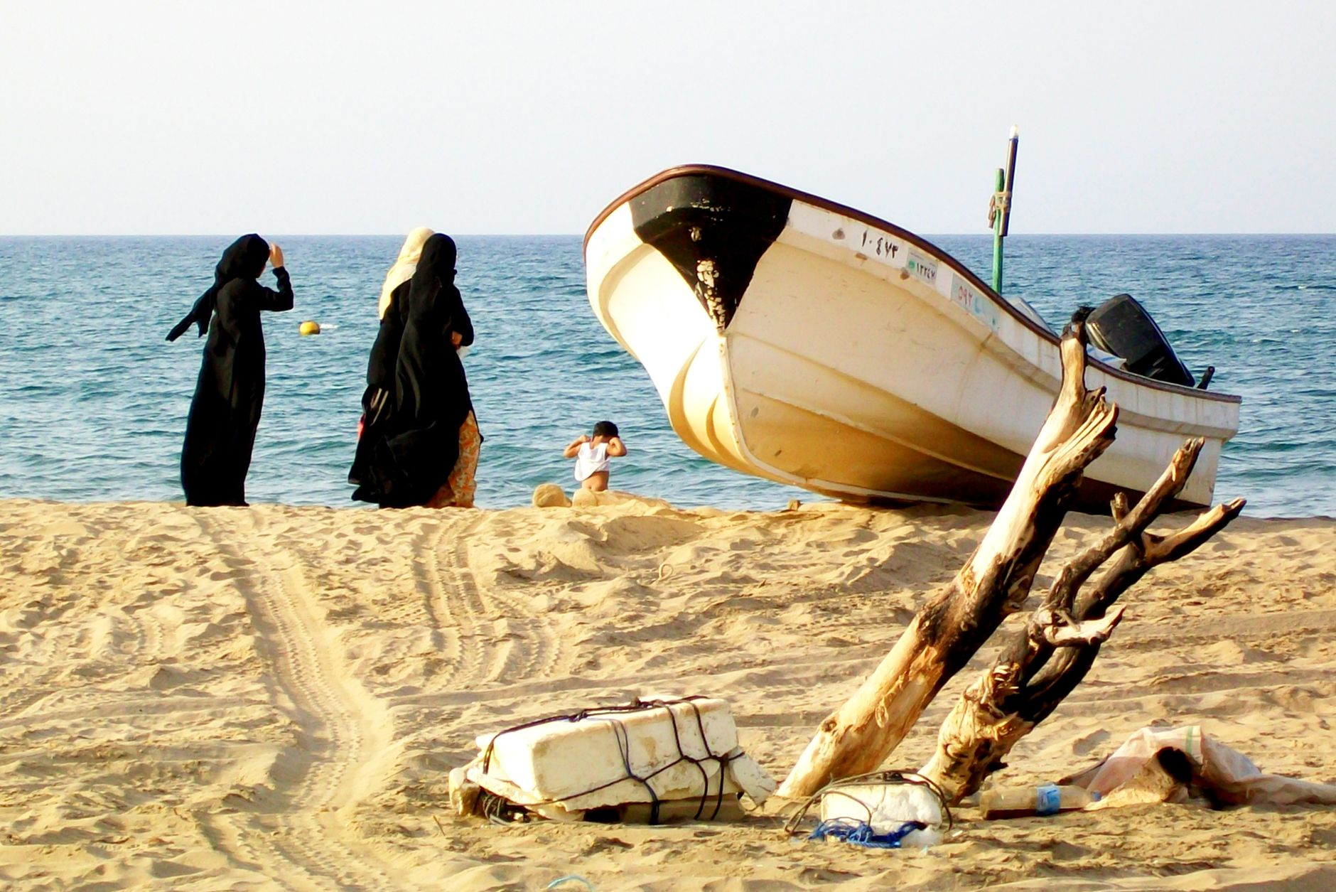 Plage de Mascate avec une barque traditionnelle et des promeneurs, Oman