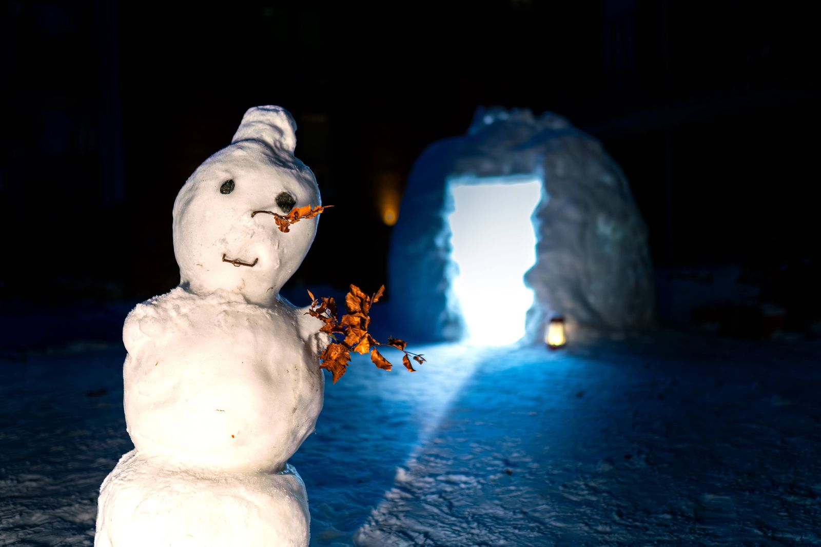 Igloo illuminé la nuit avec un bonhomme de neige devant, sous un ciel d'hiver