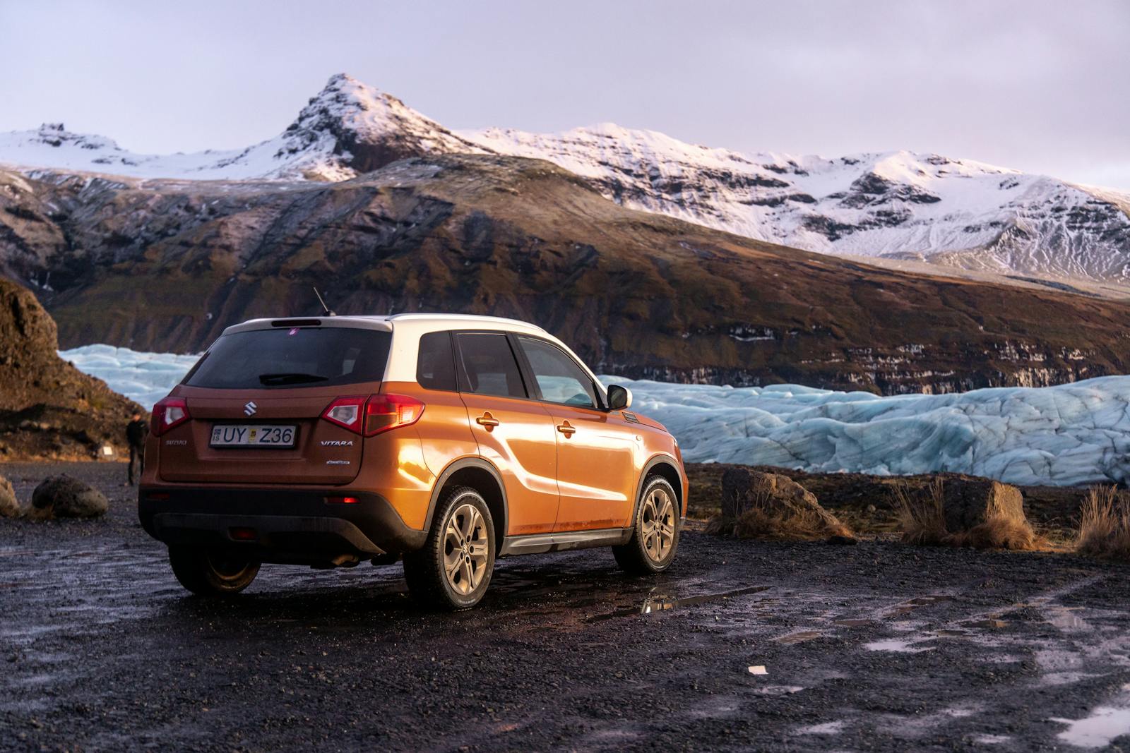 SUV orange garé devant un glacier islandais entouré de montagnes enneigées