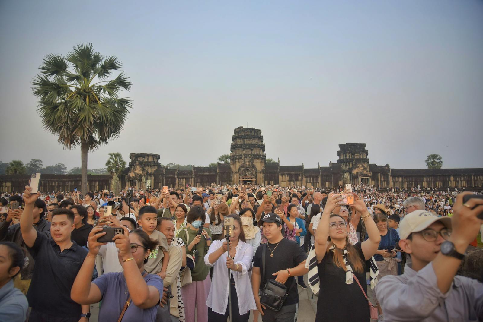 Foule dense de visiteurs smartphone à la main devant Angkor Wat au lever du soleil