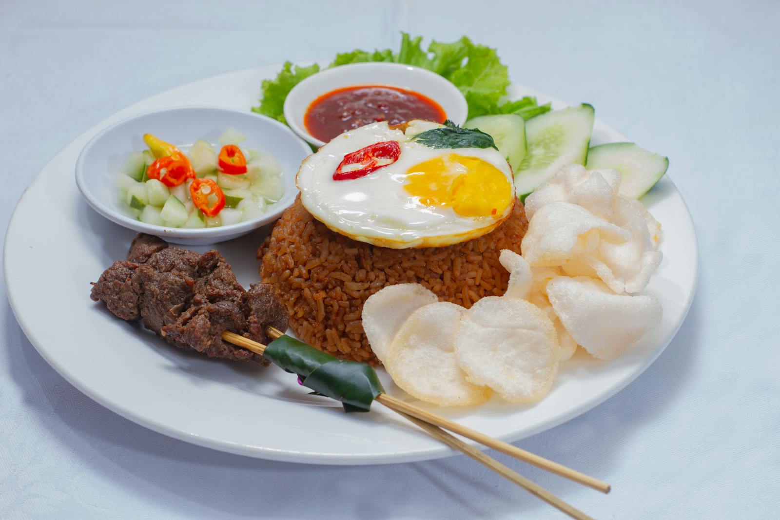 Assiette de nasi goreng servie avec œuf au plat, brochettes de satay et crackers