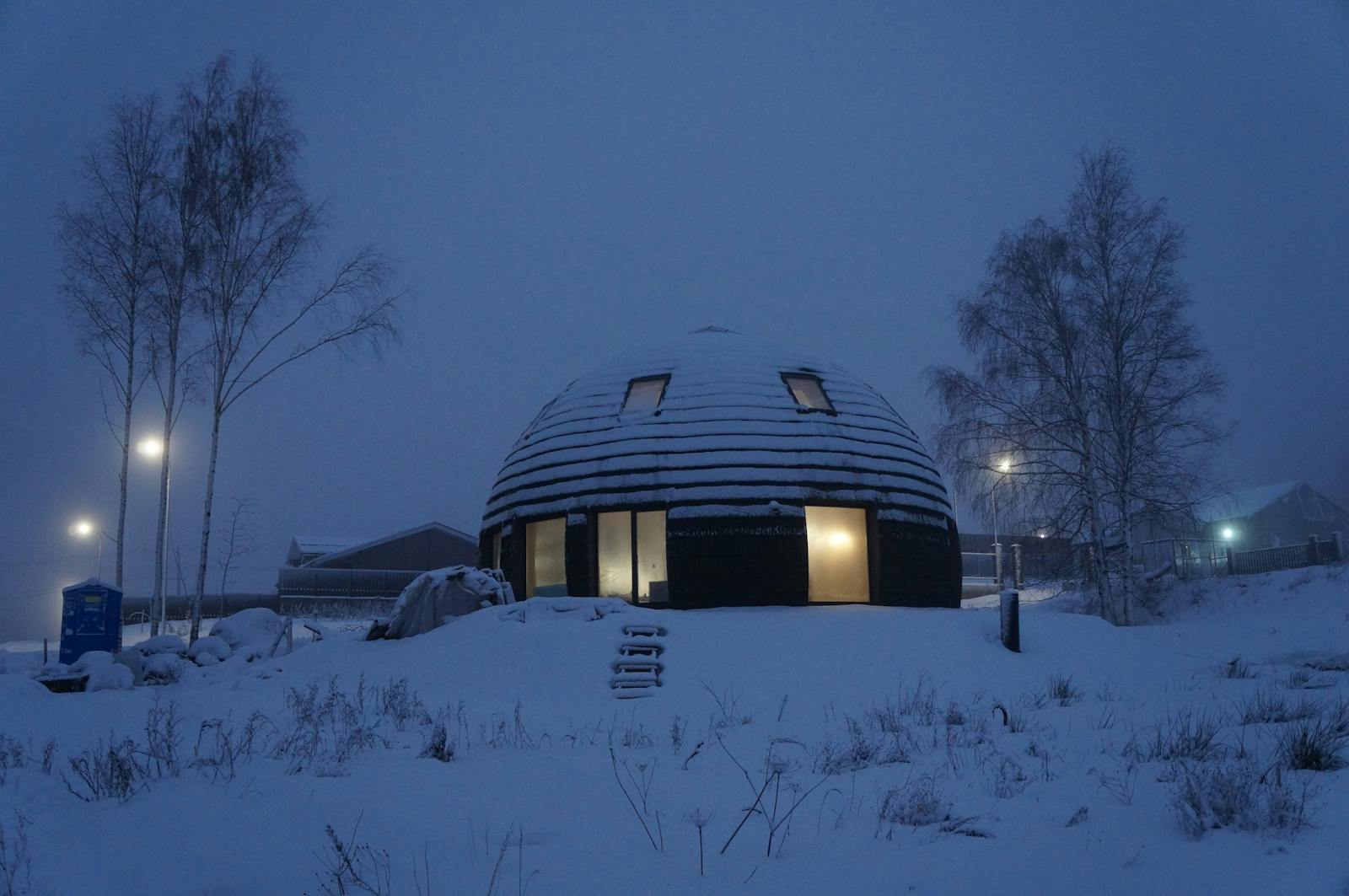 Cabane en forme de dôme illuminée dans un paysage hivernal enneigé au crépuscule