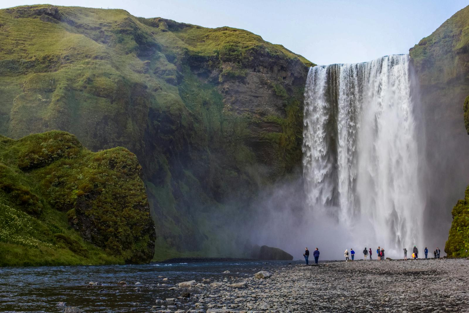 Cascade de Skógafoss en Islande avec falaises verdoyantes et visiteurs en contrebas